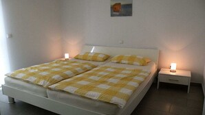 Uma cama de casal com colcha xadrez, duas mesas de cabeceira com luminárias e um pequeno quadro na parede.