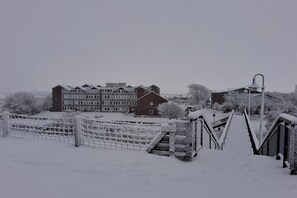 A snow-covered bridge with a metal railing, leading to a building with multiple windows and a brick facade. - with dike and North Sea view North Beach (Nordstrand)