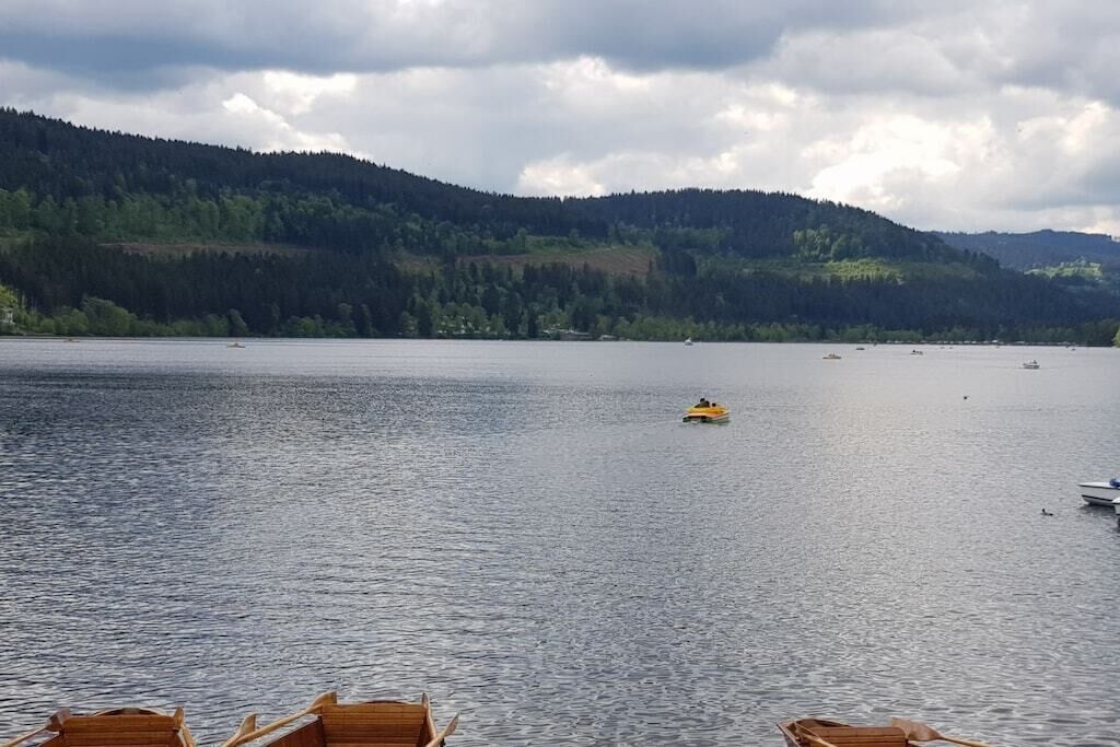 Tyyni järvi, jossa on veneitä, ja järveä ympäröivät metsäiset kukkulat.