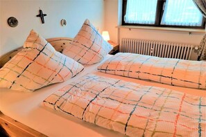 Ein Doppelbett mit kariertem Überwurf und passenden Kissen, ein Nachttisch mit Lampe, ein Heizkörper und ein Fenster mit Vorhängen.