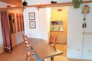 Ein Essbereich mit Holztisch und Stühlen, im Hintergrund eine Küche und eine Wanduhr.
