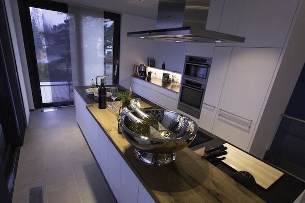 A modern kitchen with a large metallic bowl, a wine bottle, and a bottle of olive oil on the counter.