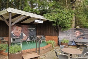 An outdoor seating area with metal chairs and tables, a covered section with a sign, and a wall with portraits and text. - Holiday apartment with 2 bedrooms (Goslar\/Hahnenklee)