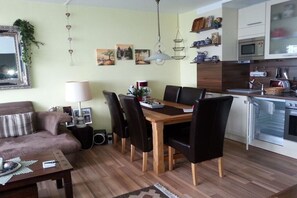 A compact living space with a dining table, chairs, a sofa, a lamp, a kitchen area with a microwave, and a refrigerator. - Holiday apartment with 2 bedrooms (Goslar\/Hahnenklee)