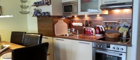 A compact kitchen with white cabinets, a microwave, an oven, and a sink.