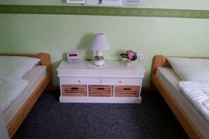 A hotel room with two single beds, a bedside table with a lamp, a small plant, and a digital clock. - Holiday apartment with 2 bedrooms (Goslar\/Hahnenklee)