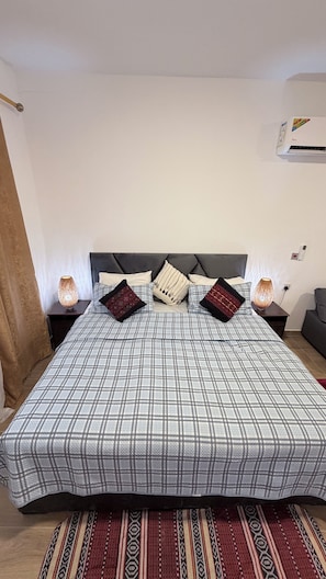 A neatly made bed with a checkered bedspread, two decorative pillows, and two bedside lamps on a nightstand.