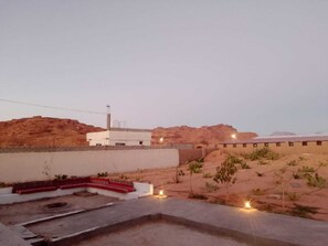 Paisatge desert amb un edifici blanc, una zona pavimentada amb escales i vegetació escassa.