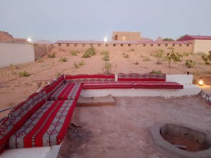 A courtyard with a seating area featuring patterned cushions, a small fire pit, and a view of a building with a red roof.