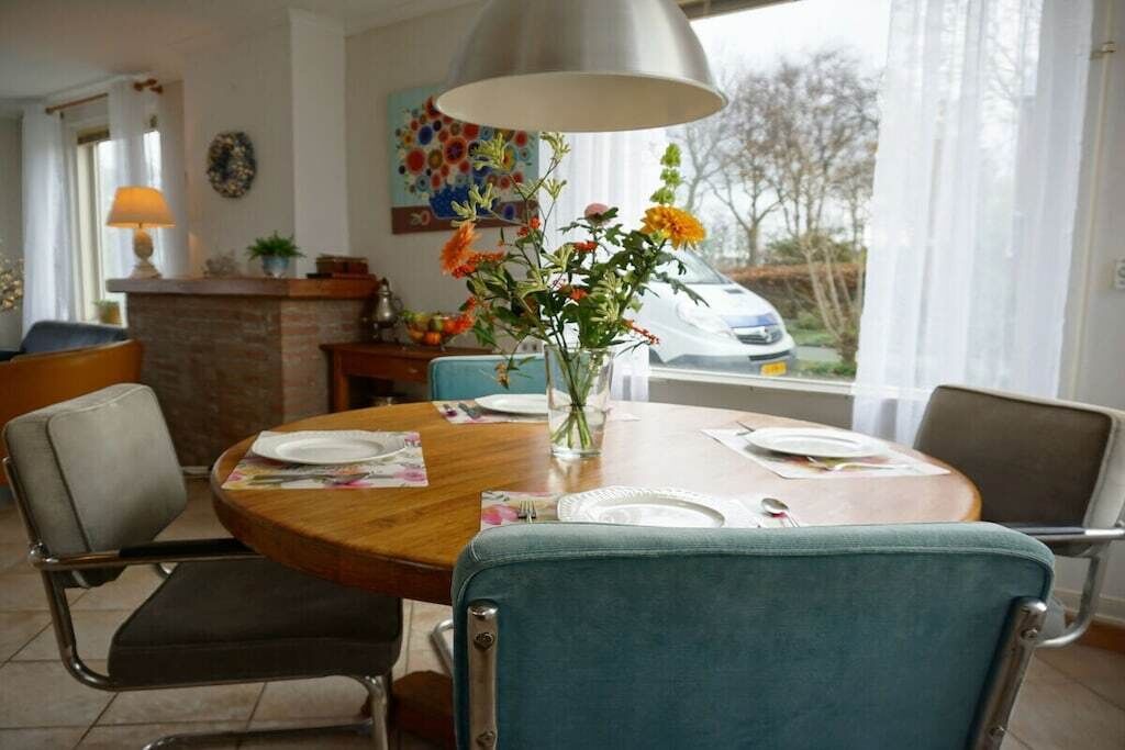 A dining area with a round table, chairs, a vase with flowers, and a view of the outside.