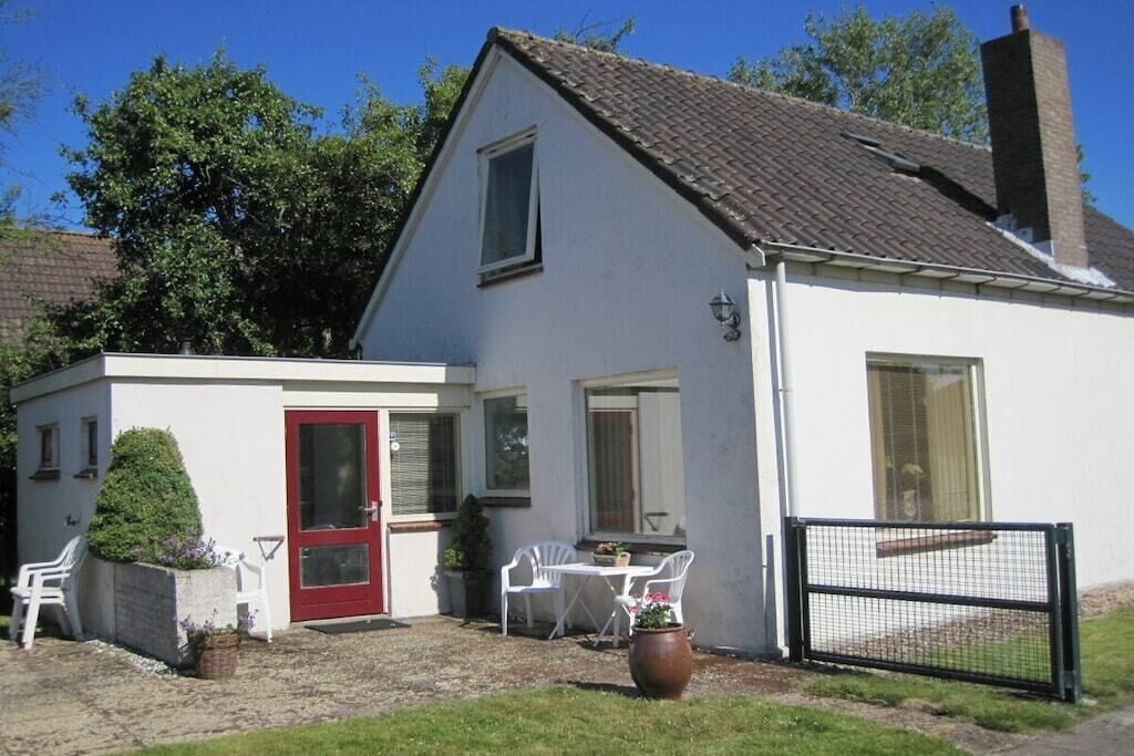 A two-story house with a red door, white exterior, and a small patio area with outdoor furniture.