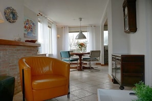 A room with a brick fireplace, a dining table with chairs, a hanging light fixture, and a clock on the wall. - Holiday home in Breezand with swimming pool (Breezand)