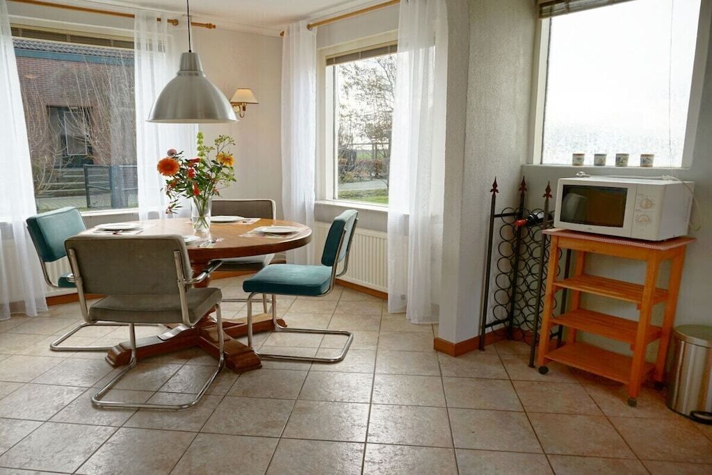 Spiseområde med et rundt bord, stole, en vase med blomster, en hængende lampe og en mikroovn på en hylde.