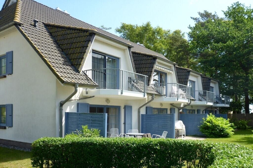 En toetages boligbygning med saddeltag, balkoner og en lille terrasse med udendørs møbler.