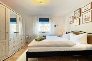 A bedroom with a bed, a wardrobe, a window with curtains, and framed pictures on the wall. - Holiday apartment with 1 bedroom (Dierhagen)