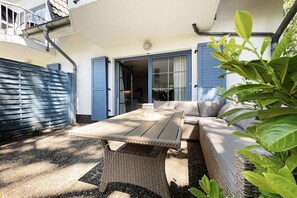 An outdoor seating area with a table and sofa, a covered patio, and a view of the interior through a glass door. - Holiday apartment with 1 bedroom (Dierhagen)