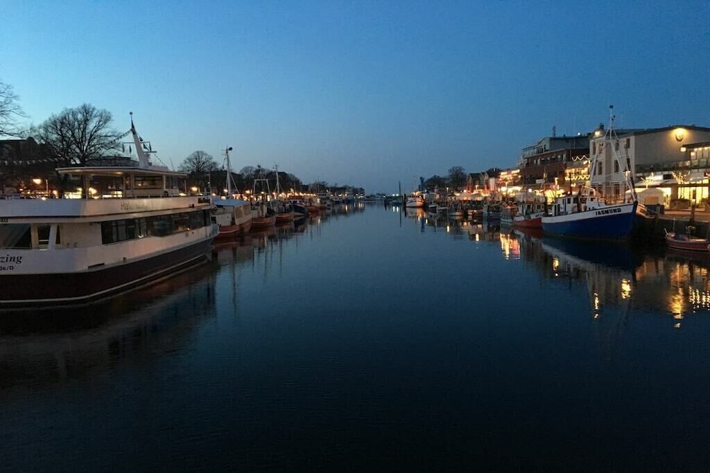 Ein ruhiger Fluss mit an beiden Ufern vertäuten Booten, umgeben von Gebäuden und einem klaren Himmel.
