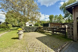 A paved courtyard with a wooden fence, a white building, and a tree. - Holiday apartment with 1 bedroom (Dierhagen)