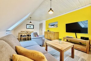 A living room with a sofa, a coffee table, a TV, and a dining area with chairs and a table. - Holiday apartment with 1 bedroom (Dierhagen)