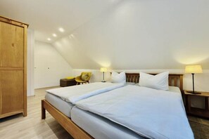 A bedroom with a large bed, two bedside tables with lamps, a wooden wardrobe, and a small chair. - Holiday apartment with 1 bedroom (Dierhagen)