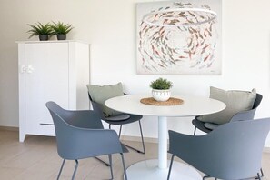 A dining area with a round table, four chairs, a white cabinet, and a wall-mounted painting. - House on the beach, Apartment 1 (Scharbeutz)