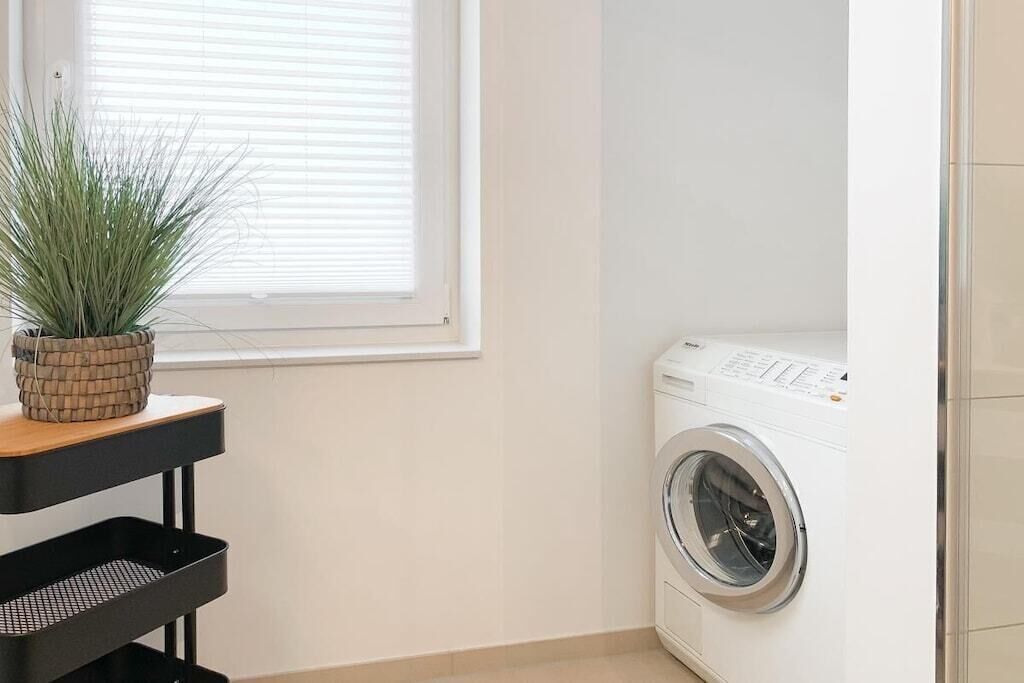A laundry room with a washing machine, a potted plant, and a black metal rack.