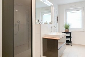 A modern bathroom with a glass shower door, a sink with a mirror, and a window with blinds. - House on the beach, Apartment 1 (Scharbeutz)