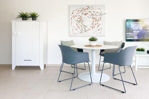 A modern dining area with a white cabinet, two grey chairs, a round table, and a hanging abstract painting. - House on the beach, Apartment 1 (Scharbeutz)