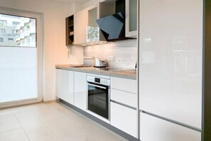 A modern kitchen with white cabinetry, a built-in oven, and a window with blinds. - House on the beach, Apartment 1 (Scharbeutz)
