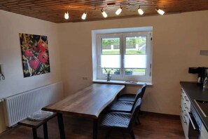 Una cocina con una mesa de madera, dos sillas, una ventana con persianas y un radiador.