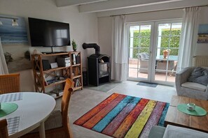 A living room with a television, a fireplace, a dining area, and a view through the glass doors. - Holiday home with 1 bedroom (Wangerland Hooksiel)