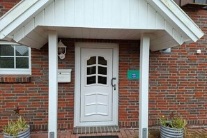 A white door with a glass panel, a small window to the left, and a green sign with a symbol on the brick wall. - Holiday home with 1 bedroom (Wangerland Hooksiel)