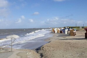 A beach with a row of beach huts and a metal railing along the shore. - Holiday home with 1 bedroom (Wangerland Hooksiel)