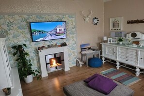 Ein Wohnzimmer mit Kamin, einem an der Wand befestigten Fernseher, einem weißen Schrank und einem blauen Sitzsack.