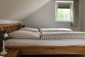 A single bed with a wooden headboard, two pillows, a bedside lamp, and a window with curtains. - Holiday home with 1 bedroom (Rheinsberg OT Flecken Zechlin)