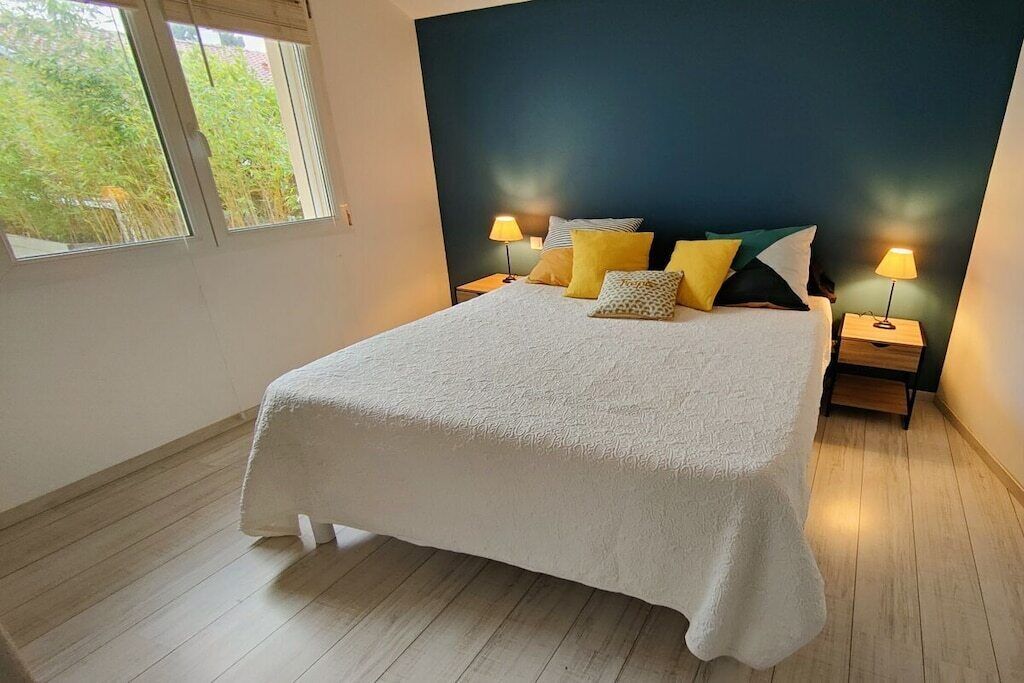A bedroom with a large bed, two bedside tables with lamps, and a window with a view of greenery.