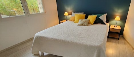 A bedroom with a large bed, two bedside tables with lamps, and a window with a view of greenery.