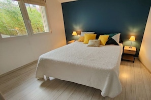 Un dormitorio con una cama grande, dos mesitas de noche con lámparas y una ventana con vistas a la vegetación.