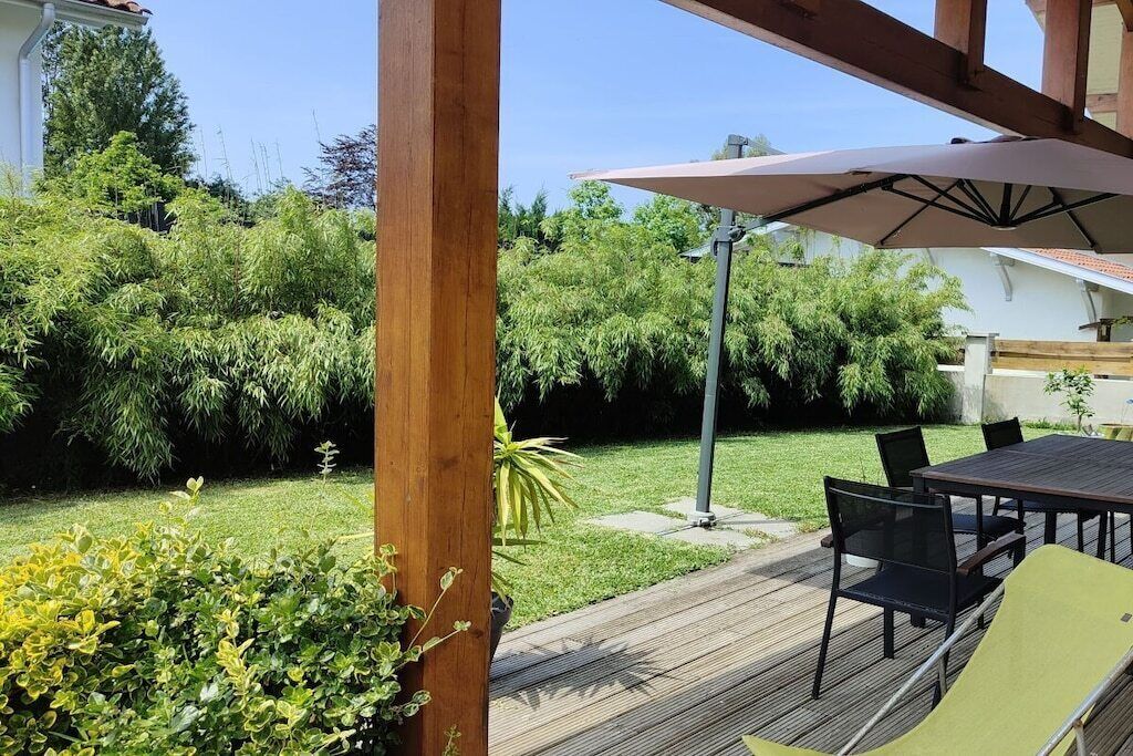 A wooden deck with a table and chairs, surrounded by lush greenery and a clear sky.