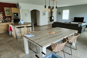 Eine moderne Küche mit einer zentralen Kochinsel, einem Essbereich mit Stühlen, einer Couch und einem Fernseher in einem Wohnbereich.
