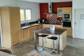 Eine moderne Küche mit Holzschränken, einer zentralen Kochinsel mit Hockern, einer Mikrowelle und einem Backofen.
