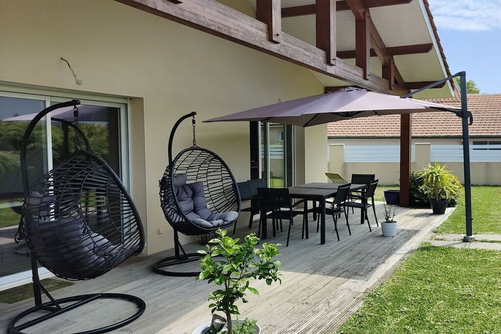 Een terras met buitenmeubilair, waaronder twee hangstoelen en een tafel met stoelen.