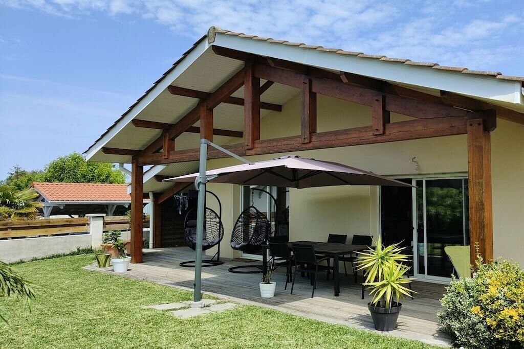 A covered outdoor patio with a table and chairs, surrounded by potted plants.