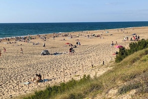 Ein sandiger Strand mit Menschen und Zelten, ein klarer Himmel und das Meer im Hintergrund.