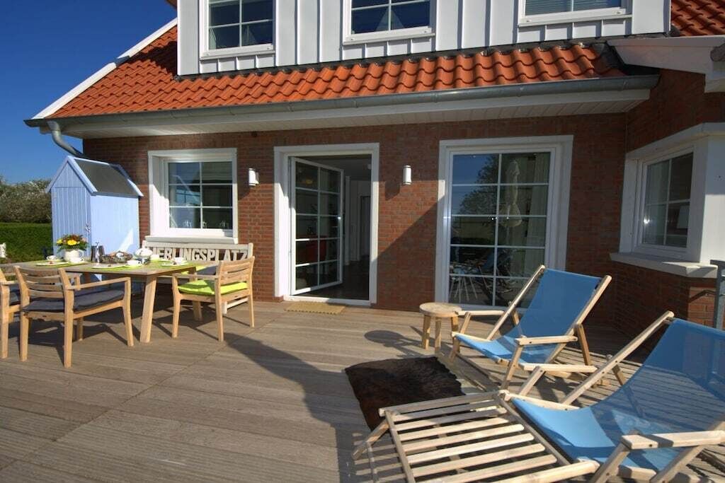 Een huis met een terras, een eethoek met stoelen en een tafel, en een overdekte zithoek met loungestoelen.