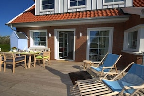 Ein Haus mit einer Terrasse, einem Essbereich mit Stühlen und Tisch sowie einem überdachten Sitzbereich mit Liegestühlen.