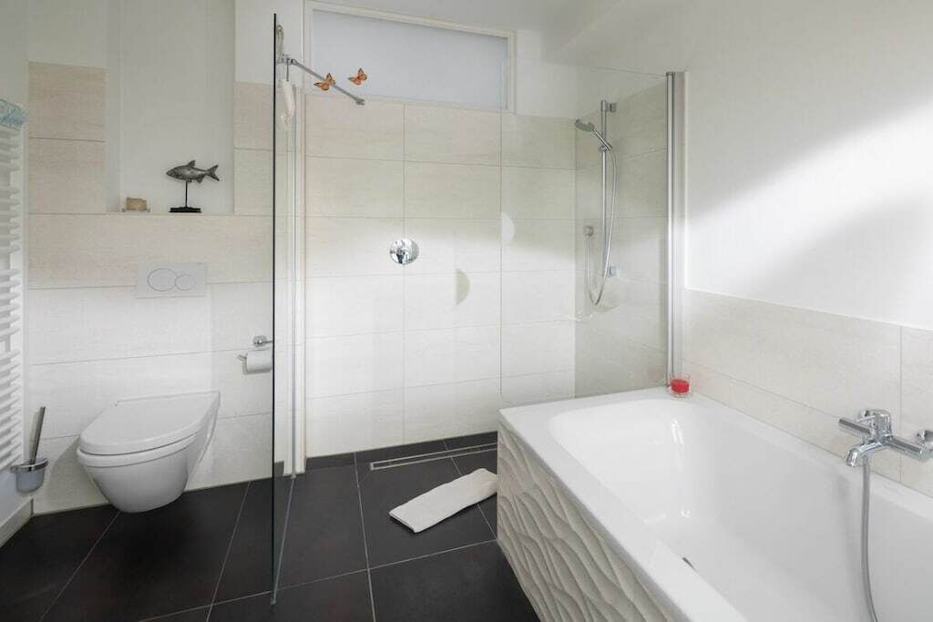Een badkamer met een witte badkuip, een douche met glazen wanden, een toilet en een klein plankje met een visdecoratie.