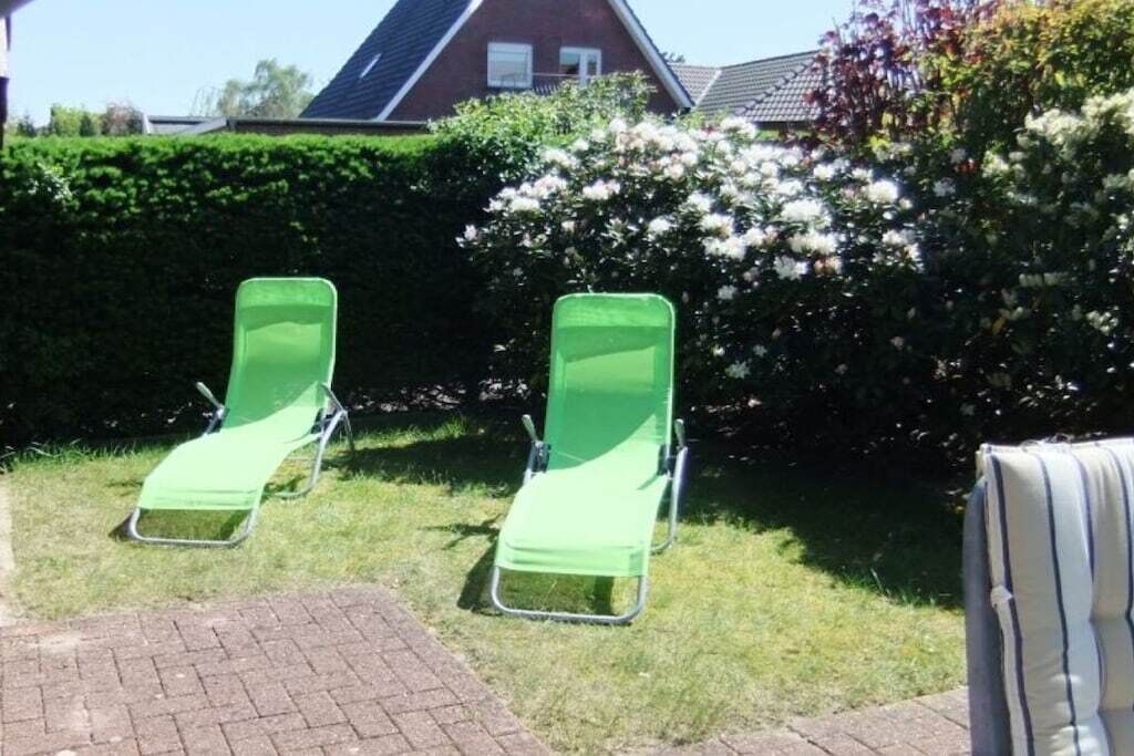 Deux chaises de jardin vertes sont placées dans un espace aménagé, avec une haie et une maison en arrière-plan.
