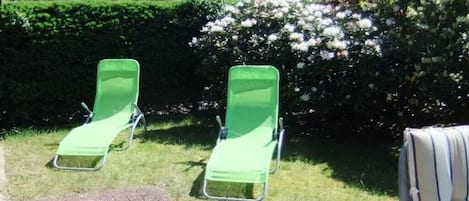 Deux chaises de jardin vertes sont placées dans un espace aménagé, avec une haie et une maison en arrière-plan.
