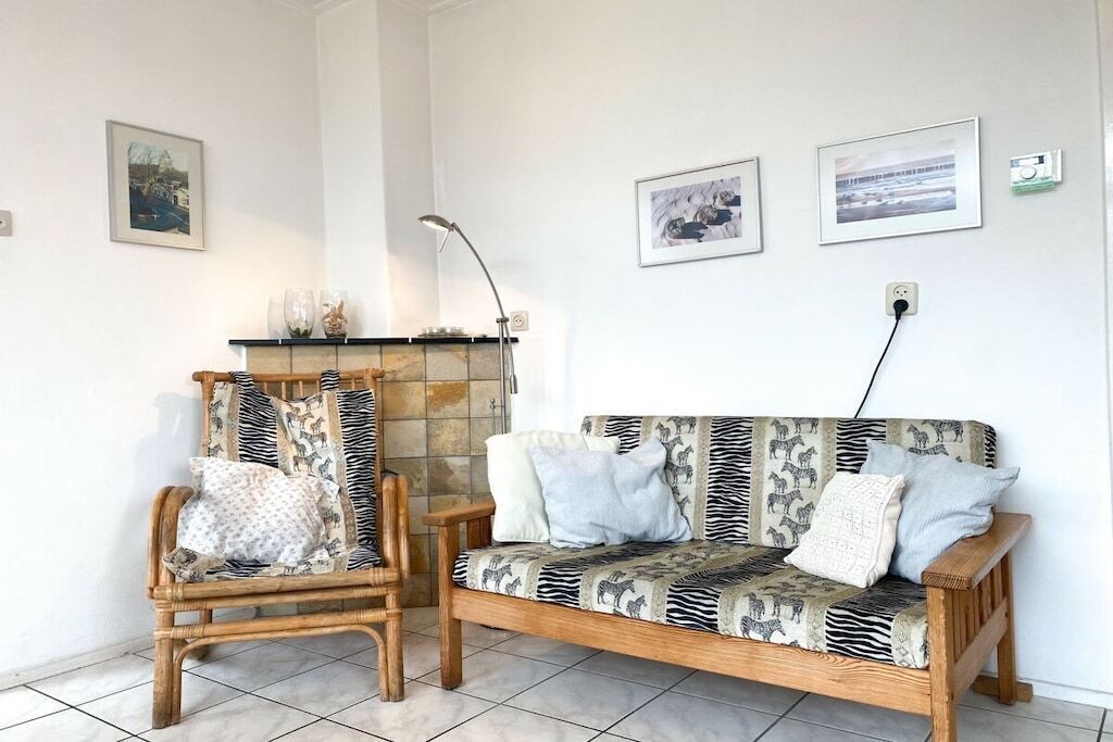 Une pièce avec un canapé et un fauteuil en bois, une cheminée et des tableaux encadrés accrochés au mur.